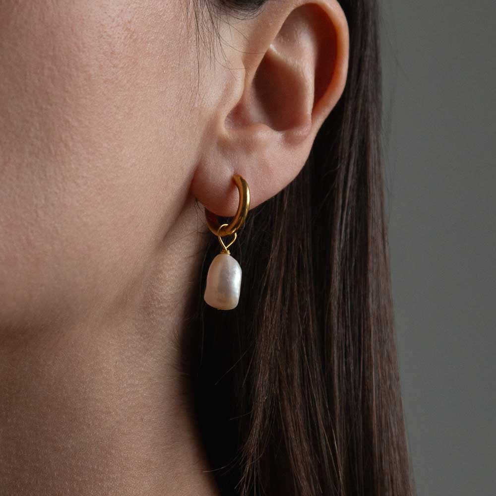 Gold hoop earring with pearl charm drop worn in ear