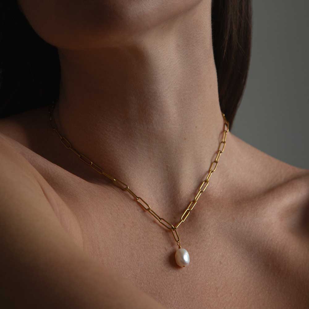 Woman’s neck wearing gold link chain with Pearl hanging from it