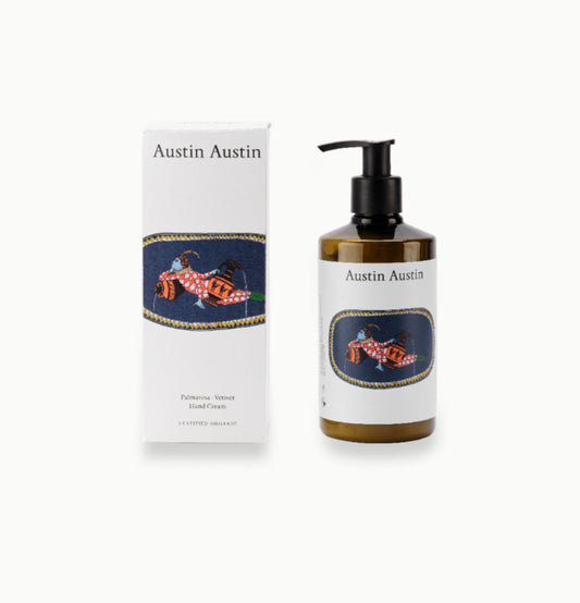 Brown bottle of hand cream with black pump lid and white label with art work and Austin Austin printed in black next to box with art work and the words Palmarosa vetiver hand cream certified organic