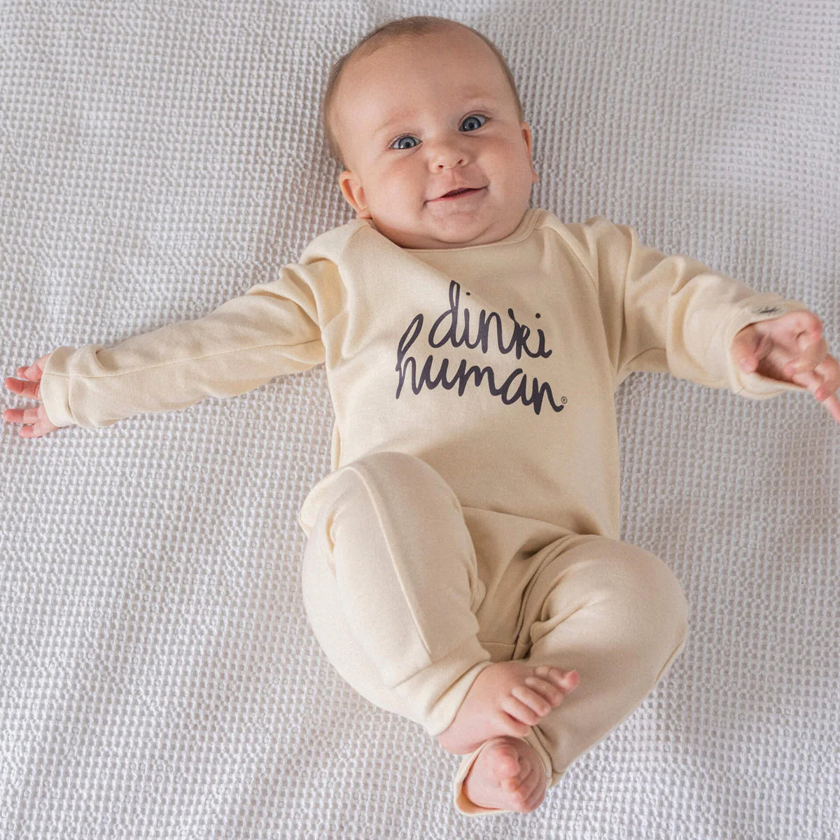 Baby wearing cream footless Babygro with Dinki Human writing on front