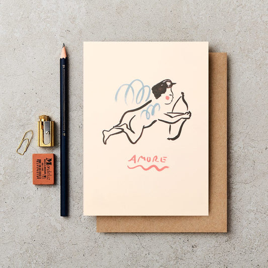 Pale blush pink cream coloured greetings card with line drawing of a cherub in black with blue swirling wings a red circle cheeks holding an bow and arrow AMORe in pink red uppercase with a wavy underline
