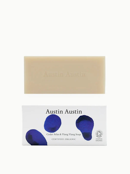 Rectangular cream coloured soap with Austin Austin printed across above a rectangular white cardboard box patterned with blue and dark blue shapes Austin Austin printed in black Cedar Atlas & ylang ylang soap CERTIFIED ORGANIC soil association logo COSMO ORGANIC