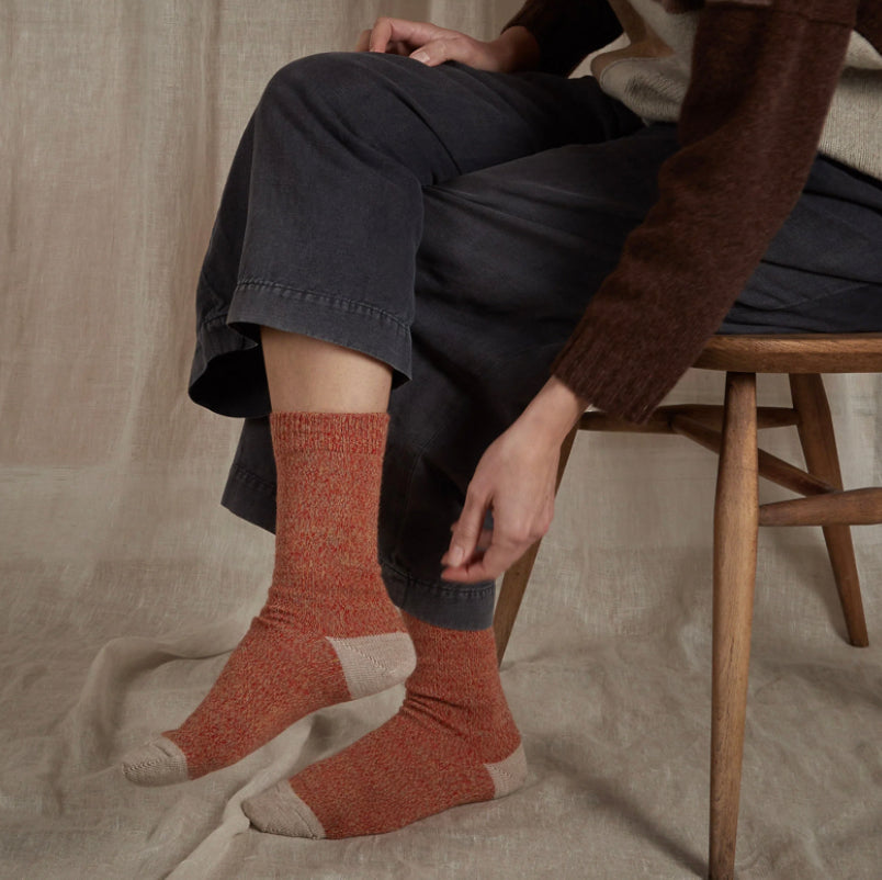 Merino sock orange fire size and beige speckled marled with beige heel size 42-46 uk 8-11 83% merino wool 17% nylon made in Britain person sat on wooden chair with navy cropped trousers with linen draped in background