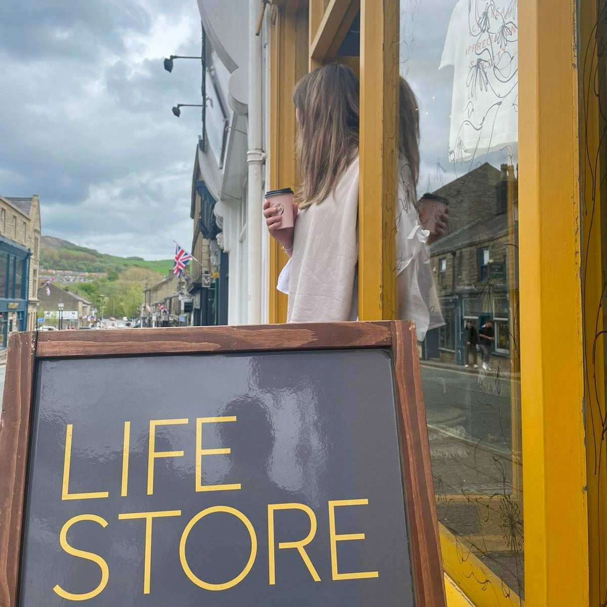 Shop owner holding coffee cup looking out of front door onto street