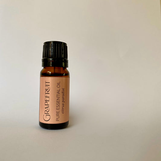 Small amber coloured glass bottle of essential oil with black lid and pink orange label with grapefruit pure essential oil citrus paradisi printed in dark grey